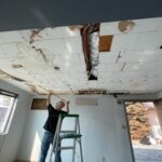 Technician repairing water-damaged ceiling during restoration